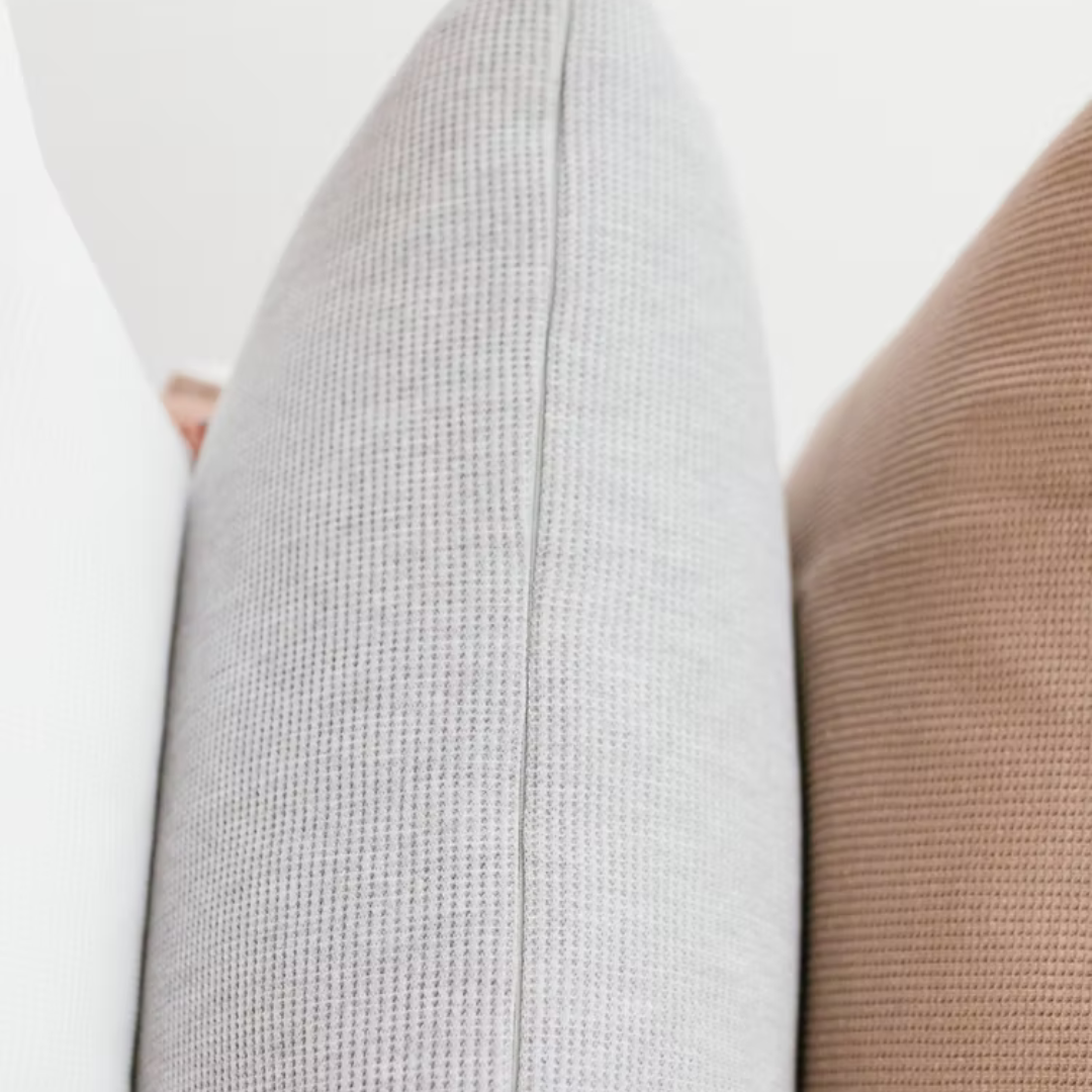 כריות נוי וופל מכותנה אורגנית מסודרות בשורה, ומציגות את צבעי הקולקציה: לבן שלג, אפור מלאנג' וחום שוקו.